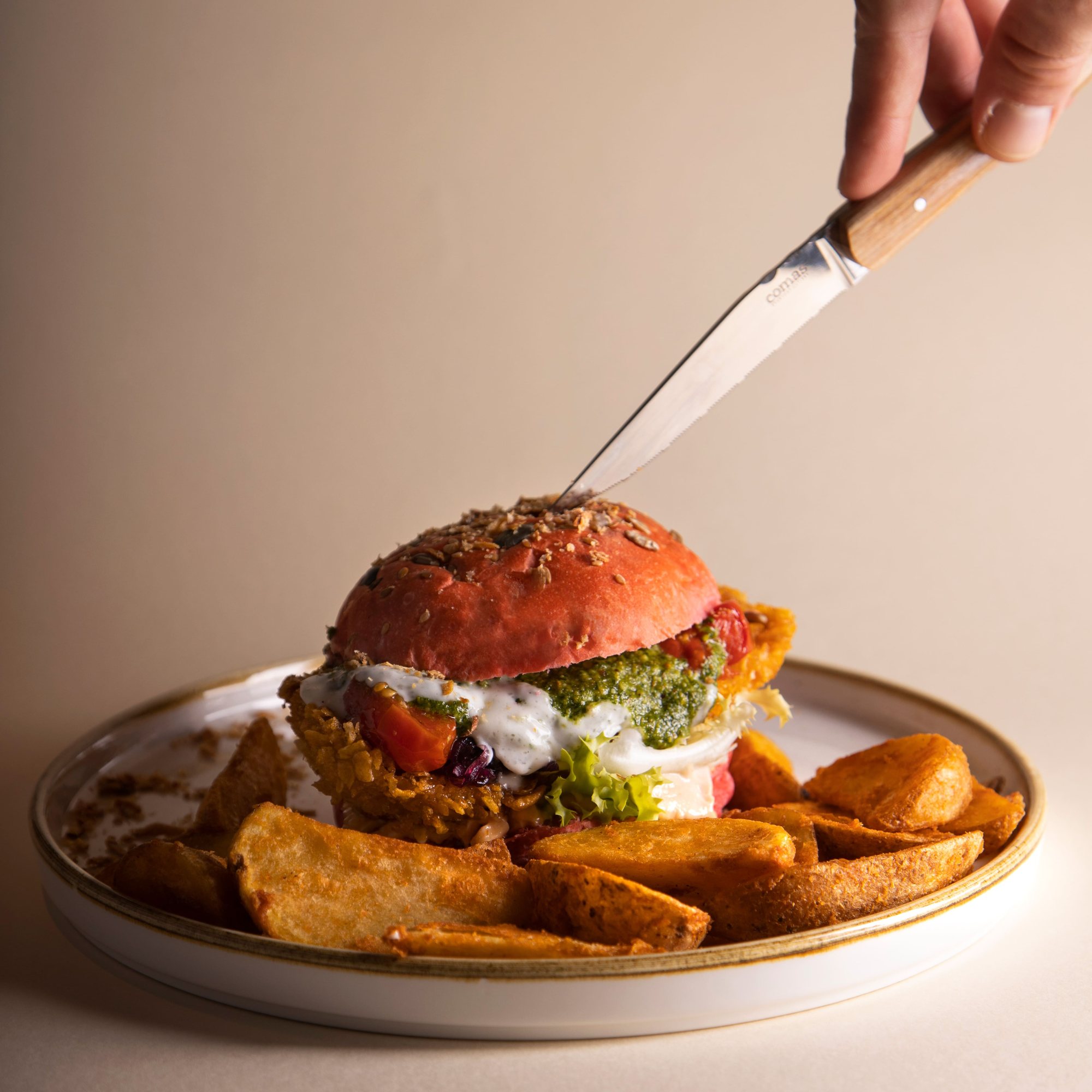 Coltello che affonda in un burger con bun rosso, servito con patate